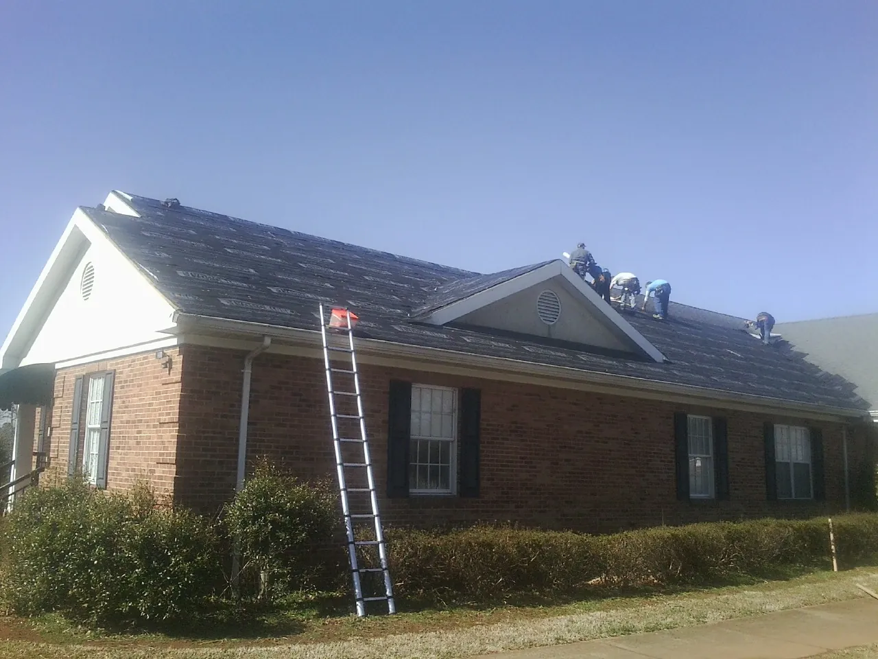 Crew tearing shingles off a brick ranch roof with a ladder set — Emergency Roof Repair work by our crew in Otis