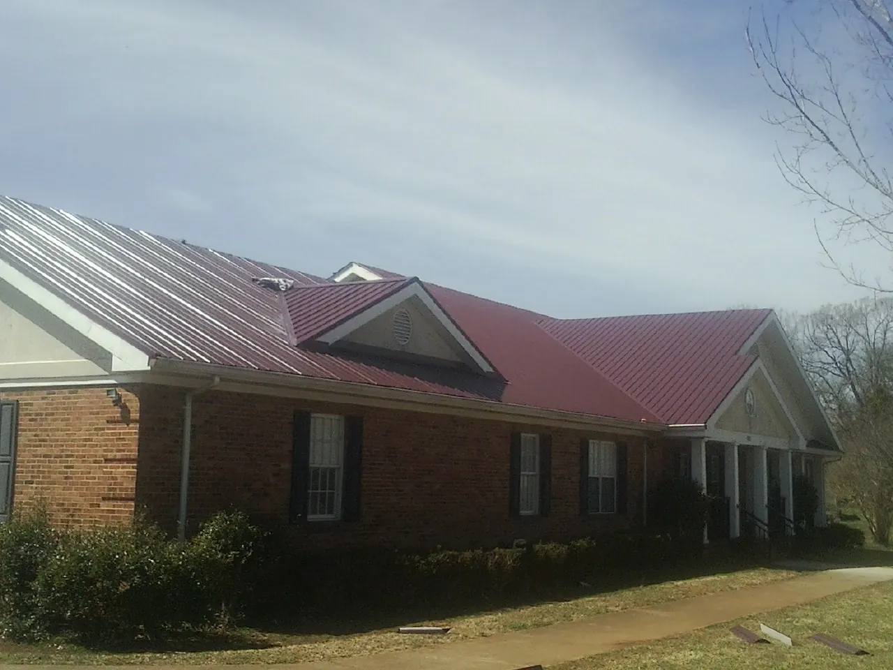 Red metal roof with gabled entries on a long brick building, from a Hail Damage Roof Repair job in Otis