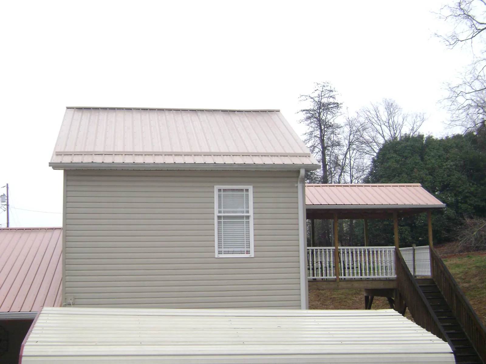 Tan metal roofs on a two story addition and attached porch, from a Roof Replacement job in Otis
